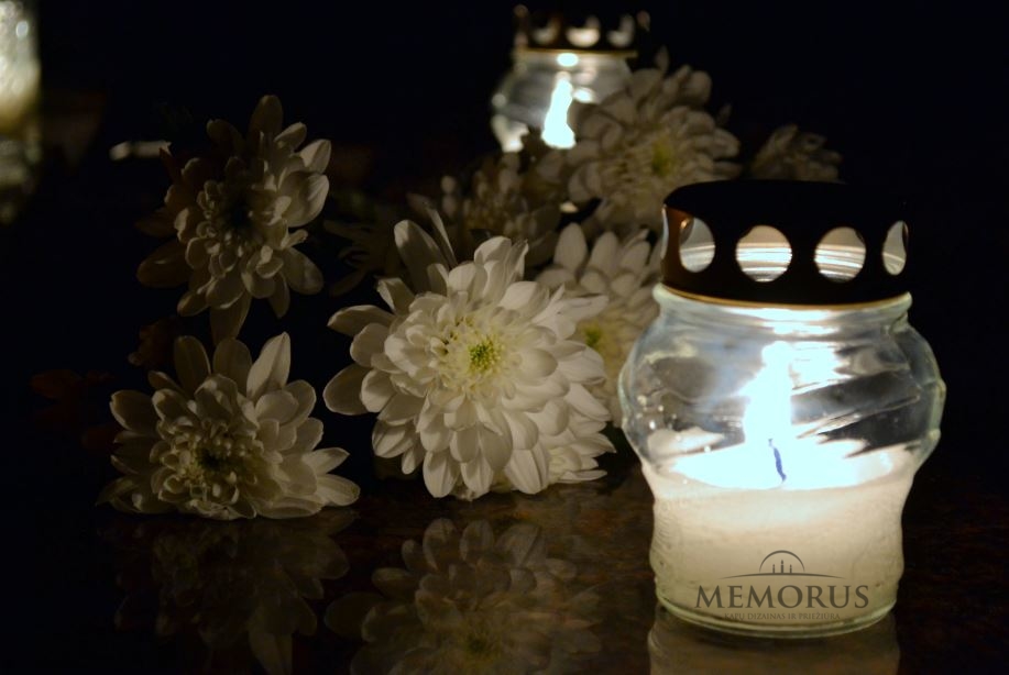 Ant kapo padėtos baltos gėlės ir uždegta žvakė