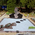 kapas užpiltas pilka skaldele ir dekoruotas granito gėlynu su akmens pėdutėmis ir augalais