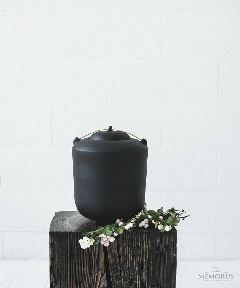 juoda kremavimo urna ant kojeliu su medienos elementu
